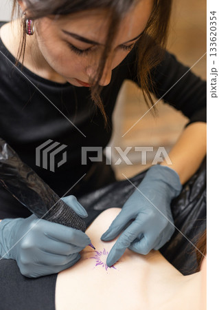 tattoo artist working on a woman chest design in a studio, showing the process of professional tattooing, precision, sterile gloves and cosmetic procedure atmosphere. 133620354