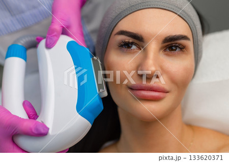 Woman receiving IPL facial treatment with a professional using a handheld device in a beauty clinic. Woman receiving IPL facial treatment with a professional using a handheld device in a beauty clinic. 133620371
