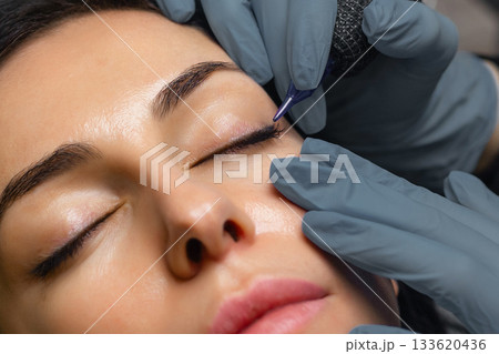 Close up of a cosmetologist performing eyelid permanent makeup, precision eyeliner tattoo procedure with sterile tools, enhancing lash line and eye beauty in a professional studio. Close up of a cosmetologist performing eyelid permanent makeup, precision eyeliner tattoo procedure with sterile tools, enhancing lash line and eye beauty in a professional studio. 133620436