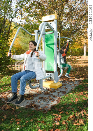 Mom and child playing sports on outdoor exercise equipment in the park. 133621165