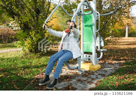 Woman Exercising on an Outdoor Fitness Machine in Autumn Park 133621166
