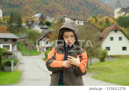 School-Age Boy Taking a Photo on His Smartphone While Walking Through an Autumn Village School-Age Boy Taking a Photo on His Smartphone While Walking Through an Autumn Village 133621276