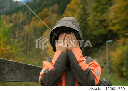 Shy Little Boy Covering His Face With His Hands While Walking Through an Autumn Park Shy Little Boy Covering His Face With His Hands While Walking Through an Autumn Park 133621280