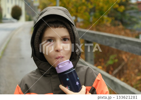A schoolchild walks around the nature and drinks water from a plastic bottle. A schoolchild walks around the nature and drinks water from a plastic bottle. 133621281