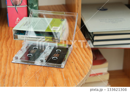 Vintage audio cassette lying among paper books on wooden bookshelf. 133621308