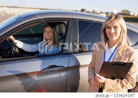 Driving Instructor Standing Near Car with Smiling Student Ready for Exam Driving Instructor Standing Near Car with Smiling Student Ready for Exam 133624197