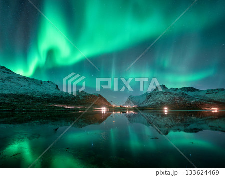 Aurora borealis over snowy mountains and calm reflective lake 133624469