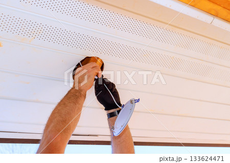 Worker is fitting light fixture to ceiling outdoors, focusing on careful installation safety. Worker is fitting light fixture to ceiling outdoors, focusing on careful installation safety. 133624471