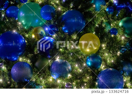 Blue, teal, and green baubles fill a Christmas tree lit with twinkle lights. The cool tones and reflections create a rich festive texture. Blue, teal, and green baubles fill a Christmas tree lit with twinkle lights. The cool tones and reflections create a rich festive texture. 133624716