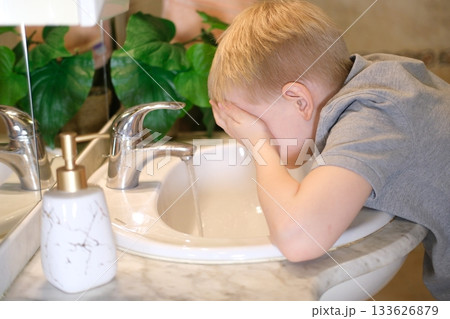 Young boy washing face in bathroom sink during morning routine Young boy washing face in bathroom sink during morning routine 133626879