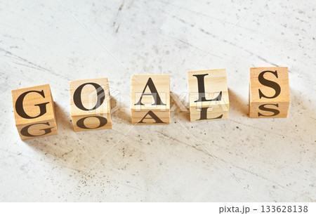 Five wooden cubes with word GOALS on white stone like board, view from above 133628138