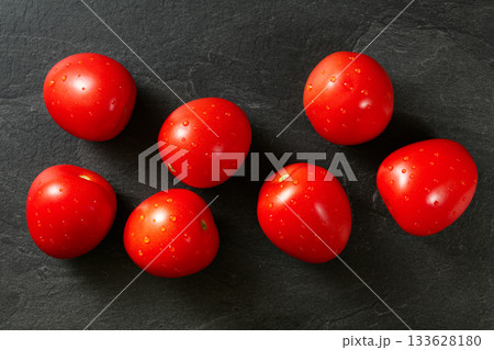 Top down view, seven mini tomatoes with drops of water on black stone desk 133628180
