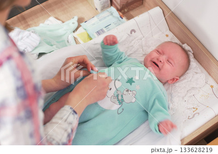 Mother changing infant baby clothes on the table, detail to boy crying 133628219