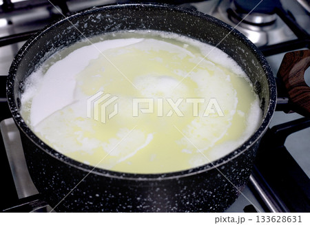 Milk curdling in pot on stove during homemade cheese making process. Fresh whey separation. Close up Milk curdling in pot on stove during homemade cheese making process. Fresh whey separation. Close up 133628631