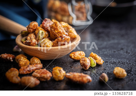 Nuts coated in sugar glaze on wooden spoon on black table. Nuts coated in sugar glaze on wooden spoon on black table. 133628718
