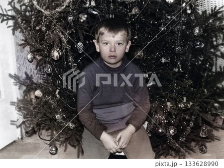 A Vintage portrait of a six-year-old boy by the Christmas tree. Retro photo from 1972. A Vintage portrait of a six-year-old boy by the Christmas tree. Retro photo from 1972. 133628990