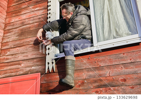 Linking power lines as installer attaches DC jack male to DC jack female during surveillance camera setup on rural home facade. 133629698