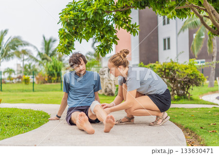 Man experiencing knee pain during outdoor workout in the park while woman provides first aid. Concept of injury care, health, wellness, safety, active lifestyle, and mindful assistance Man experiencing knee pain during outdoor workout in the park while woman provides first aid. Concept of injury care, health, wellness, safety, active lifestyle, and mindful assistance 133630471