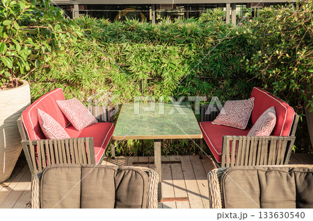 Outdoor seating area with red cushions and greenery background 133630540