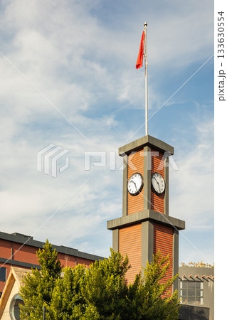 Brick clock tower with red flag and blue sky on a sunny day Brick clock tower with red flag and blue sky on a sunny day 133630554