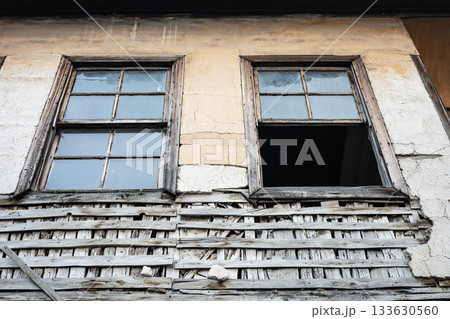 Weathered old building with broken windows and worn wooden lattice on rustic wall Weathered old building with broken windows and worn wooden lattice on rustic wall 133630560