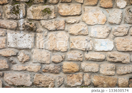 Textured stone wall with varied brick patterns and moss accents 133630574
