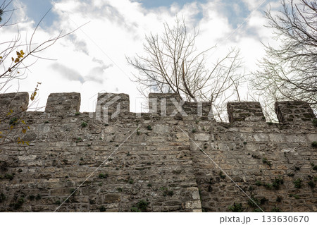 Medieval stone fortress wall with battlements under cloudy sky 133630670