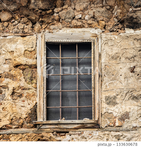 Ancient stone building with weathered wooden window frame in rustic setting 133630678