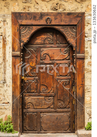 Ornate wooden door with carved patterns on rustic stone wall 133630682