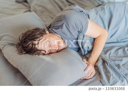 Man sleeping peacefully in his bed with gray bedding at home. Concept of rest, relaxation, healthy sleep, wellness, self-care, and comfortable lifestyle in a cozy bedroom environment 133631008
