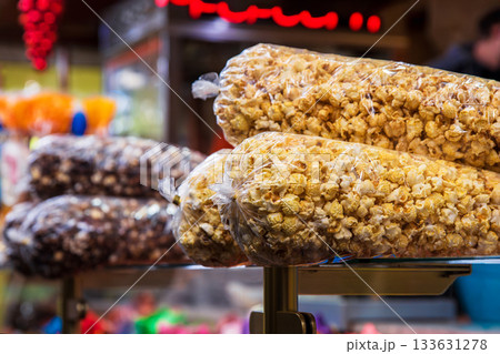 Transparent plastic bags of caramel and chocolate popcorn stacked on a stand at a festive christmas market stall. Transparent plastic bags of caramel and chocolate popcorn stacked on a stand at a festive christmas market stall. 133631278