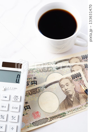 福沢諭吉の肖像の一万円紙幣と電卓、淹れたてのコーヒー 133631470