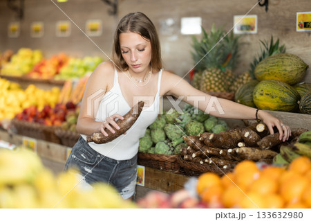 Girl shopping in grocery supermarket - choosing yucca root Girl shopping in grocery supermarket - choosing yucca root 133632980