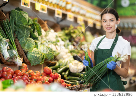 Girl shop seller add bunch of green onion goods on display case in vegetable store 133632986