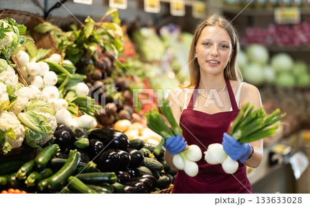 Supermarket employee carefully places green onion on shelves of grocery supermarket Supermarket employee carefully places green onion on shelves of grocery supermarket 133633028