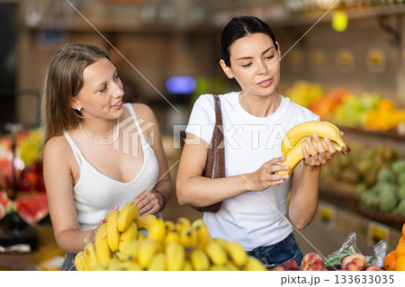Two women choosing bananas at vegetable shop Two women choosing bananas at vegetable shop 133633035