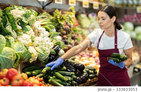 Adult woman seller puts zucchini in vegetable shop Adult woman seller puts zucchini in vegetable shop 133633053