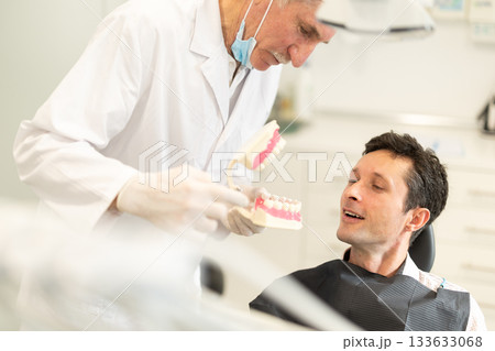 Elderly male dentist showing model of teeth to patient 133633068