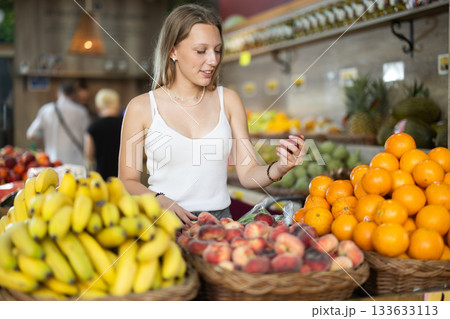 Young woman choosing flat peaches at vegetable shop Young woman choosing flat peaches at vegetable shop 133633113