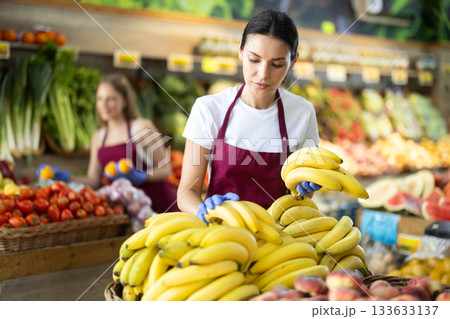 Working in supermarket - female salesman sorts through ripe bananas on display case Working in supermarket - female salesman sorts through ripe bananas on display case 133633137
