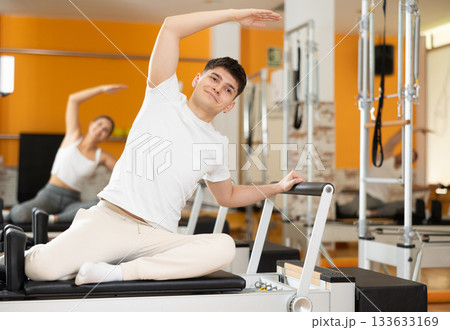 Guy doing side bend with arm extended on Pilates reformer Guy doing side bend with arm extended on Pilates reformer 133633169