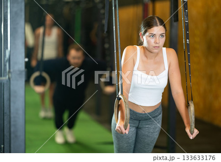 Young woman doing press-ups on gymnastic rings at gym 133633176