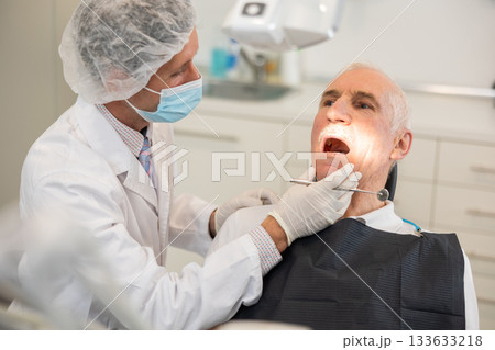 Man doctor dentist in white coat examines oral cavity of mature male patient in dentistry. Man doctor dentist in white coat examines oral cavity of mature male patient in dentistry. 133633218