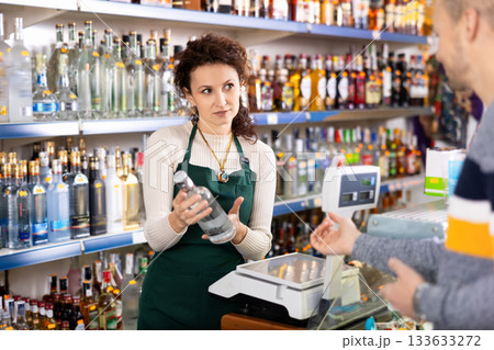 Seller recommends high-quality vodka to man buyer in alcohol department of Russian store 133633272