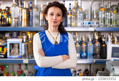 Portrait of positive saleswoman at cash register of liquor store 133633352
