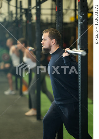 Determined young guy working out with weight rod during crossfit workout Determined young guy working out with weight rod during crossfit workout 133633371