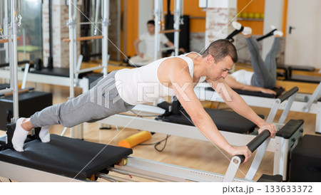 Man in different poses performs static and dynamic exercises on reformer Man in different poses performs static and dynamic exercises on reformer 133633372