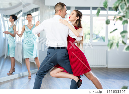 Couple in stage costumes learns tango dancing during individual lesson 133633395