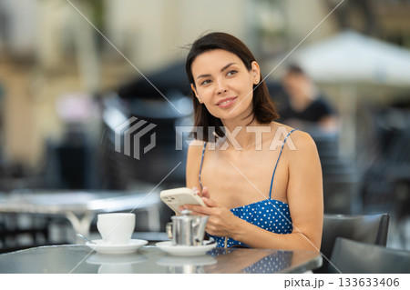 Young woman with phone drinking tea in cafe 133633406