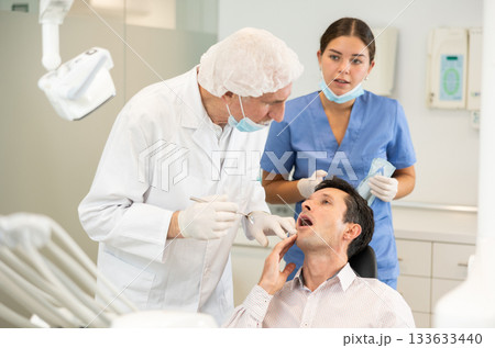 Elderly male dentist with nurse examining male patient Elderly male dentist with nurse examining male patient 133633440